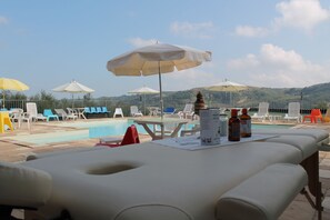 A poolside area with lounge chairs and umbrellas, a table with bottles, and a view of hills in the background.