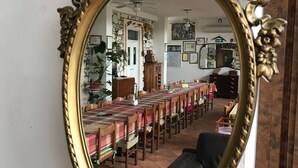 Een kamer met een grote, versierde spiegel die een eethoek met een lange tafel en stoelen weerspiegelt.