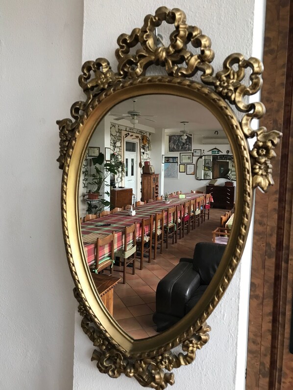 A room with a large ornate mirror reflecting a dining area with a long table and chairs.