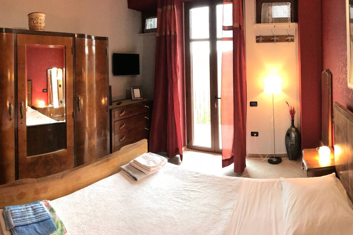 Een hotelkamer met een bed, een kledingkast, een bureau, een spiegel, een televisie en een raam met gordijnen.