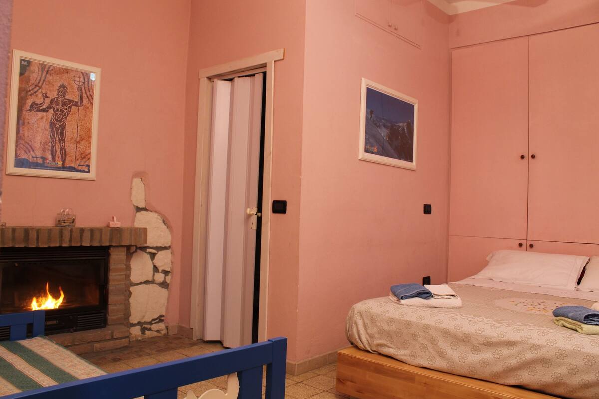 Een slaapkamer met een stenen open haard, een bed met een bloemenprint deken en een deur naar een andere kamer.