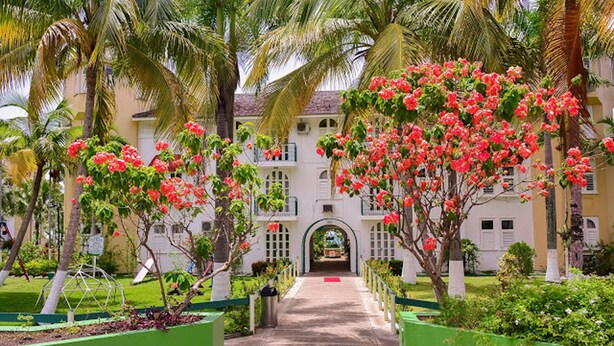 A pathway leading to a building with a white facade and green accents, surrounded by lush greenery and palm trees. - Sandy Shores at Sandcastles (Ocho Rios)