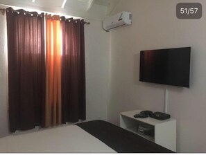 A bedroom with a bed, a TV mounted on the wall, a small white console table, and an air conditioning unit. - Sandy Shores at Sandcastles (Ocho Rios)