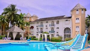 A swimming pool with slides, palm trees, and a building with multiple balconies and a tower. - Sandy Shores at Sandcastles (Ocho Rios)