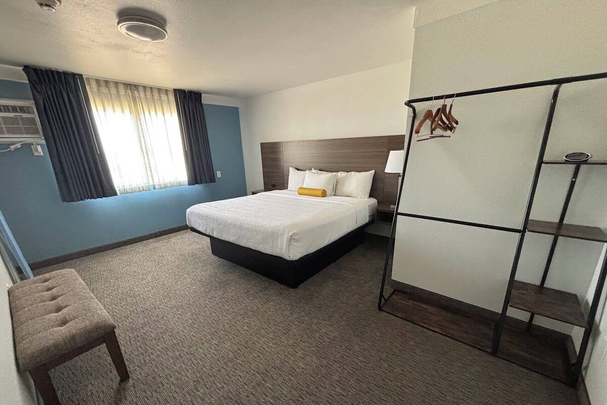 Ein Hotelzimmer mit einem Bett, einem Nachttisch, einem Kleiderschrank und einem Fenster mit Vorhängen.