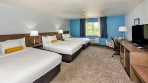 Ein Hotelzimmer mit drei Betten, einem Schreibtisch mit Fernseher und einem Fenster mit Vorhängen.