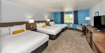 Habitación de hotel con tres camas, un escritorio con televisor y una ventana con cortinas.