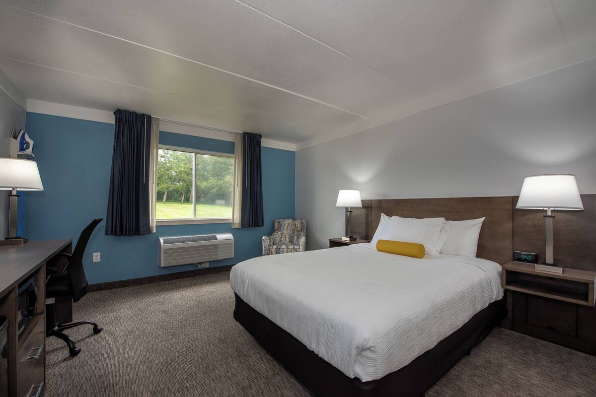 Ein Hotelzimmer mit einem großen Bett, zwei Nachttischen mit Lampen, einem Schreibtisch mit Stuhl, einem Fenster mit Vorhängen und einer Klimaanlage.