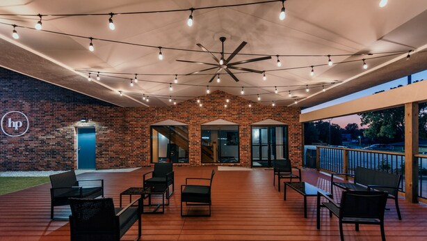 Eine Terrasse im Freien mit Ziegelmauern, Deckenventilatoren, Lichterketten und Gartenmöbeln.