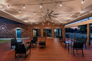 Un patio al aire libre con paredes de ladrillo, ventiladores de techo, luces colgantes y mobiliario exterior.