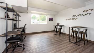 A modern office space with a wooden floor, metal shelving, a desk with a laptop, and two chairs.