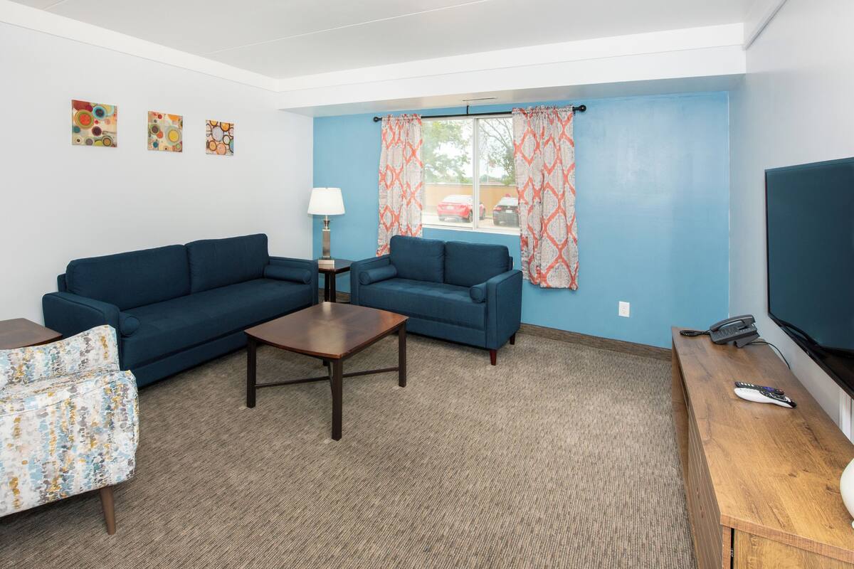Ein Wohnzimmer mit zwei blauen Sofas, einem kleinen Holztisch, einer Lampe und einem Fernseher auf einem Holzständer.