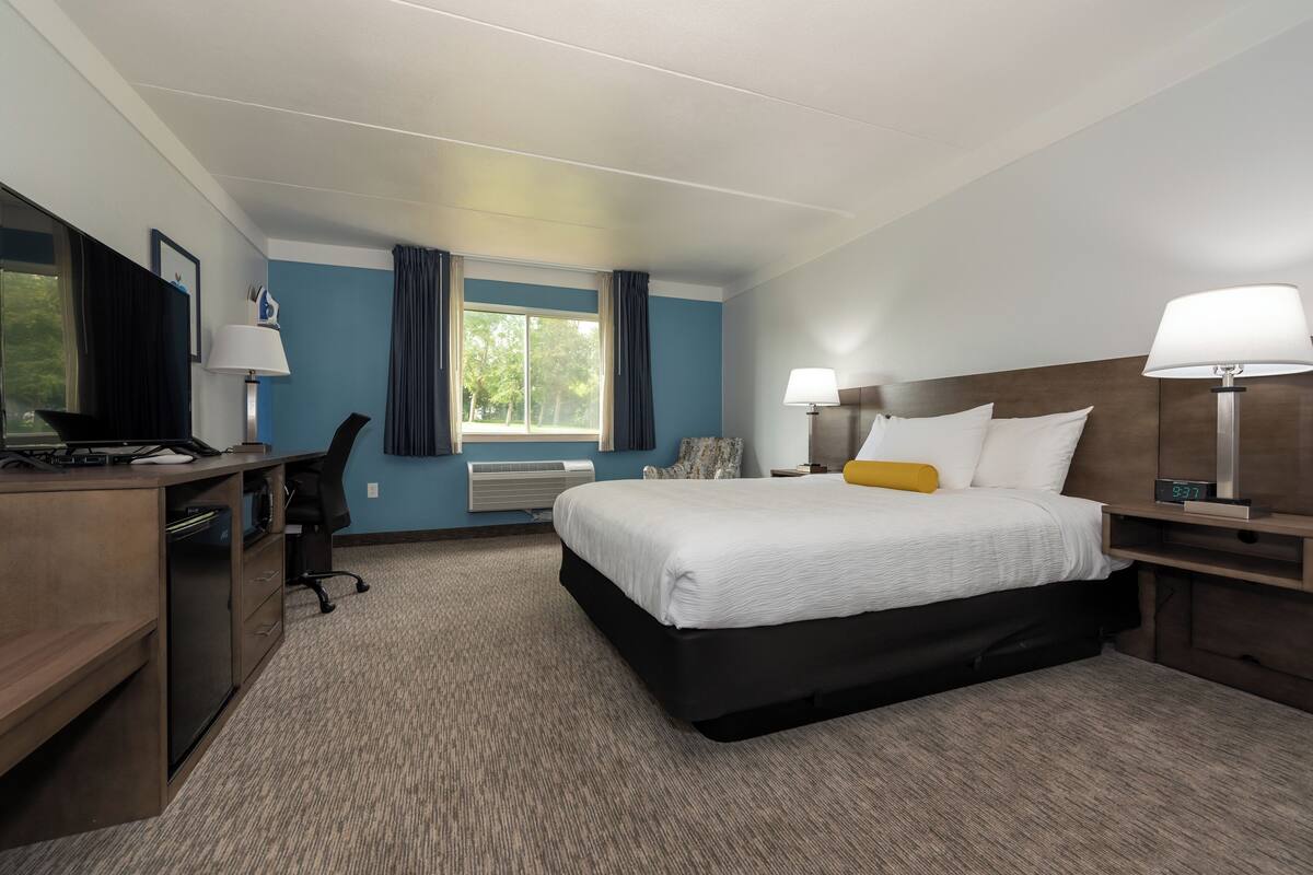 Ein Hotelzimmer mit Bett, Schreibtisch, Computer und einem Fenster mit Vorhängen.