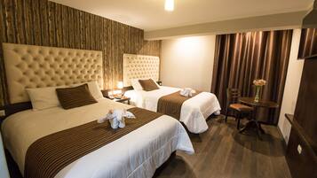 A hotel room with two beds, a wooden accent wall, a small table with chairs, and a nightstand with a lamp.