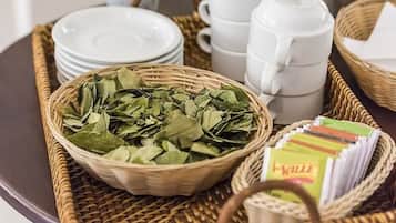 A tray with a basket of green leaves, white teapots, and stacked white plates.