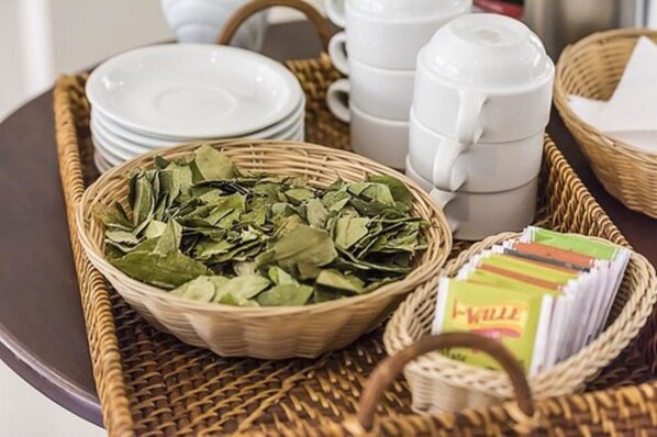A tray with a basket of green leaves, white teapots, and stacked white plates. - Ureta Hotel (Cusco)