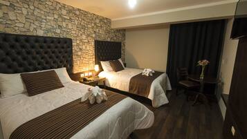 Habitación de hotel con dos camas, pared de piedra, suelo de madera, escritorio con silla y televisor de pantalla plana.