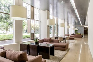 A modern hotel lobby with large windows, a central seating area, and a long corridor.