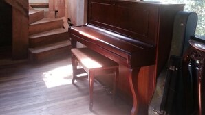 A wooden interior with a grand piano near a window, wooden stairs, and a staircase leading to an upper level. - Casa Alquimia Artes (Monteverde)