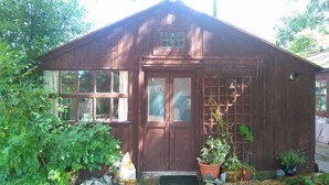 A wooden shed with a door, windows, and a small porch area with potted plants. - Pear Tree Farm (Glastonbury)
