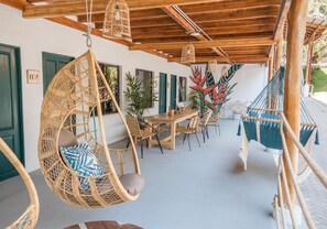 A covered outdoor seating area with wicker chairs, a hammock, and hanging light fixtures. - Socialtel Santa Teresa South (Cóbano)