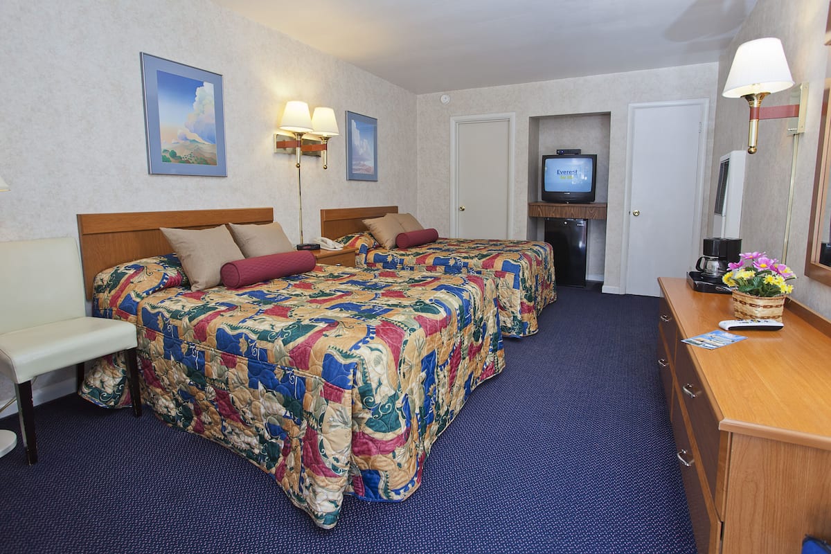A hotel room with two beds, a desk, a television, and a bathroom door.