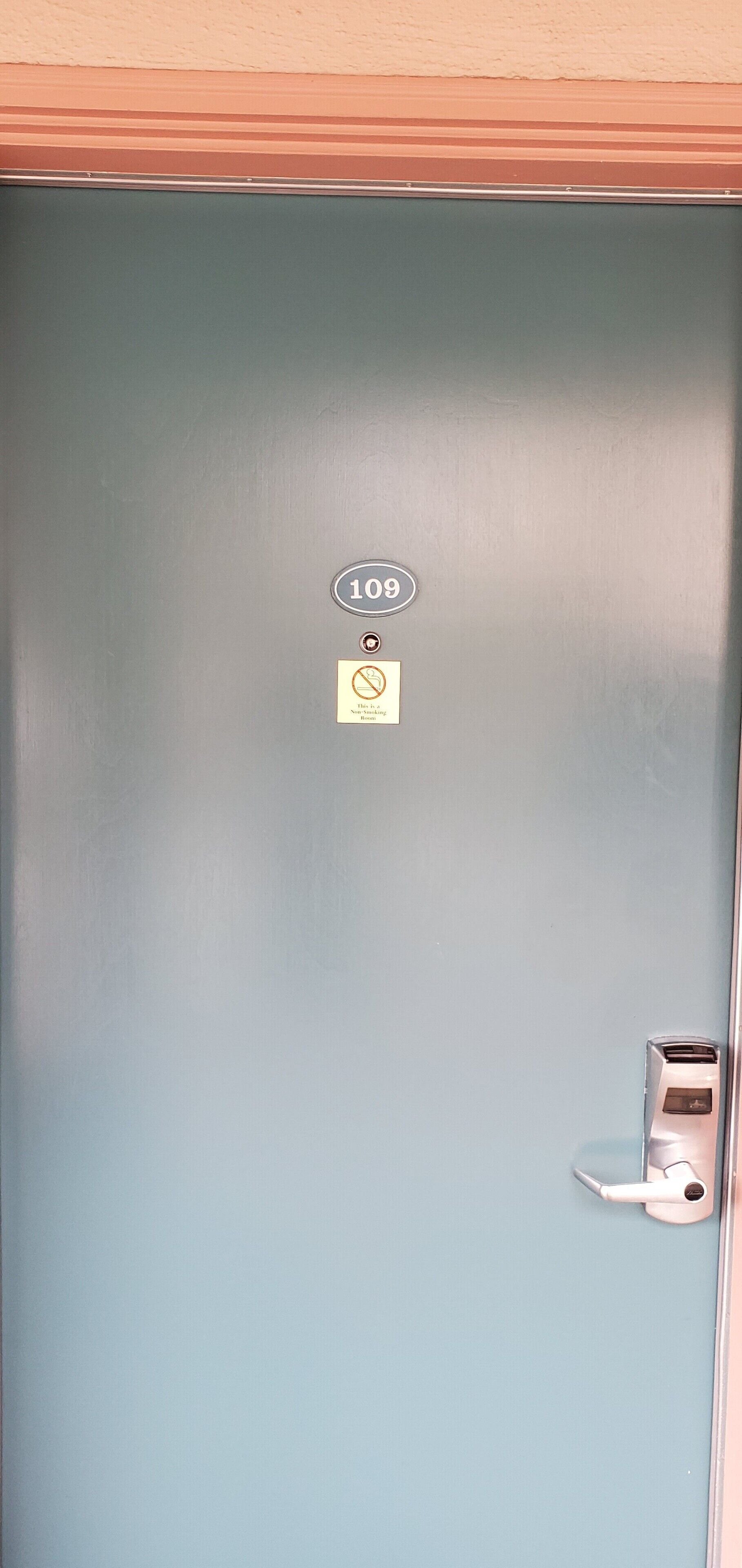 A door with a number plate, a no smoking sign, and a modern electronic lock.