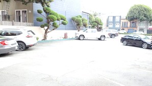 A parking lot with several cars, a building with a blue facade, and neatly trimmed trees. - Townhouse Motel (San Francisco)