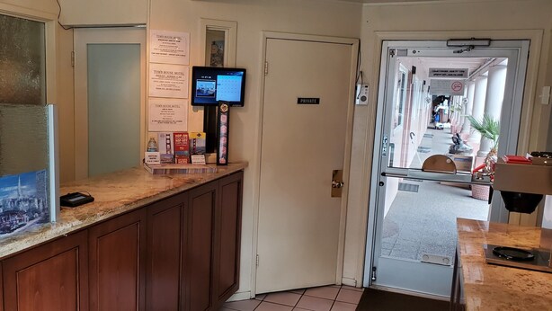 A hotel reception area with a digital screen, a private room door, and a counter with informational brochures. - Townhouse Motel (San Francisco)