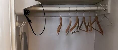 A small closet with a hanging rack, an iron, and a radiator.