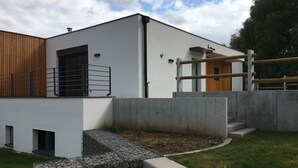 Un bâtiment moderne à la façade blanche, agrémenté d’une section à lattes de bois et doté d’un escalier en béton menant à une porte en bois.
