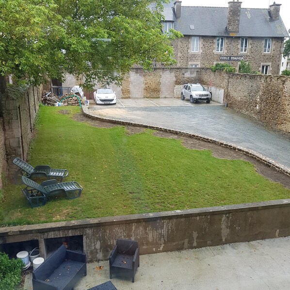 A courtyard with a paved path, green lawn, outdoor seating, and a stone building in the background.