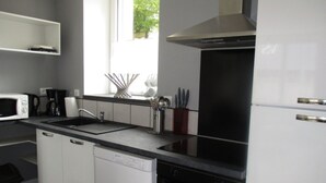 Een moderne keuken met witte kasten, een zwart aanrecht, een rvs-afzuigkap, een vaatwasser en een oven.