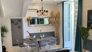 Ein modernes Wohnzimmer mit einer schwarzen Ledersofa, einem Essbereich mit einem Glastisch und Stühlen, und einer Küche im Hintergrund.