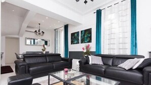 Ein modernes Wohnzimmer mit schwarzen Ledersofas, einem Glastisch und einer Chandelier.