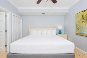 Ein Schlafzimmer mit Bett, Nachttisch, Lampe, einer Tür und einem Bild an der Wand.
