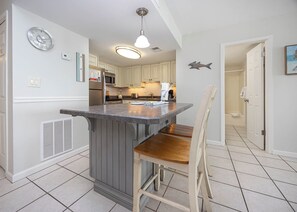 A kitchen with a central island, a microwave, and a refrigerator. There is a chair at the island and a ceiling light fixture.