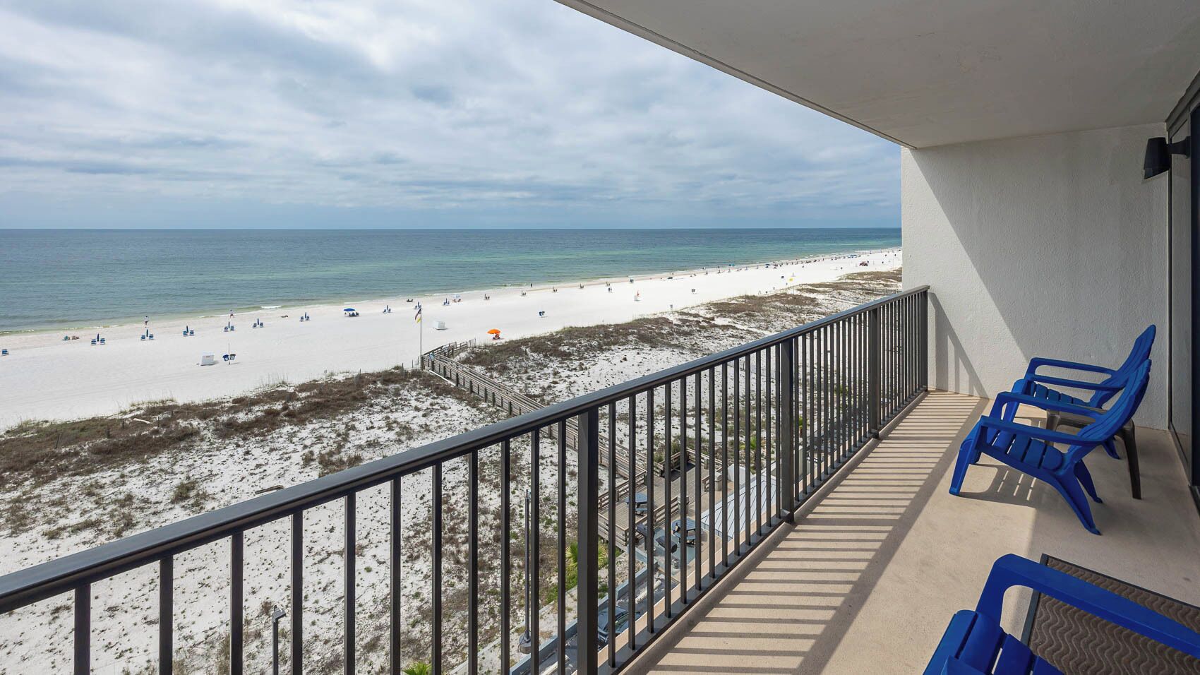Een balkon met uitzicht op een strand, met een hekwerk en blauwe stoelen.