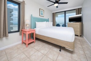 Una habitación de hotel con cama, una mesita con lámpara, cómoda, televisor y balcón con vistas.