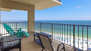 A balcony with a view of the beach, featuring green chairs and a table.