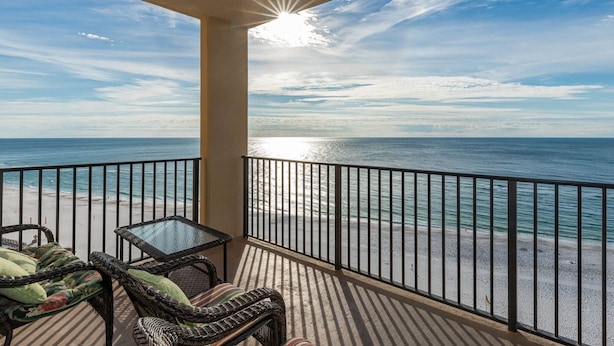 A balcony with wicker furniture and a glass table overlooking a beach with a railing. - Beautiful 2BD Gulf Front Condo - Phoenix V 1206 (Orange Beach)
