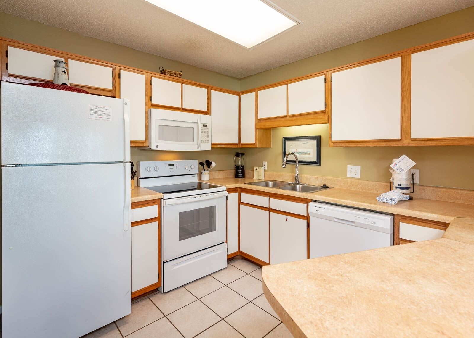 A compact kitchen with white appliances, wooden cabinets, and a tiled floor.
