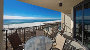 A balcony with a view of the beach, a glass table, and wooden chairs. - 3rd Floor ~ One Bedroom - Phoenix III (Orange Beach)