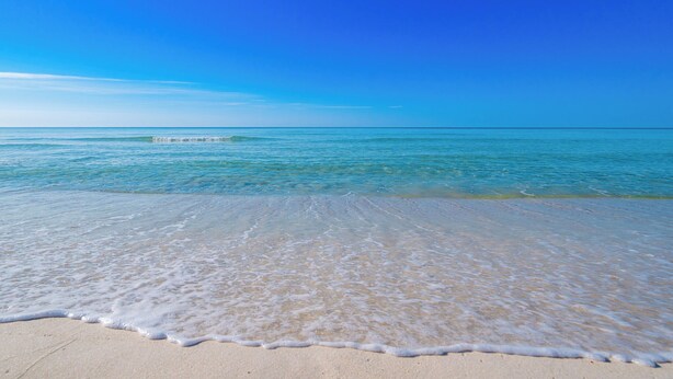 A beach with clear blue water and a sandy shore.