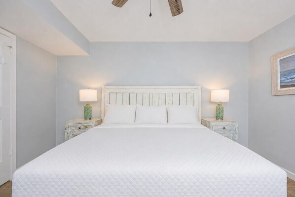 Un dormitorio con una cama blanca, dos mesitas de noche con lámparas, un cabecero de madera y un cuadro enmarcado en la pared.