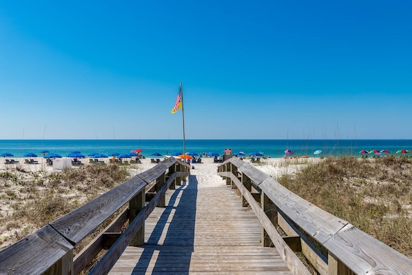 A wooden boardwalk leading to a beach with umbrellas and beach chairs.