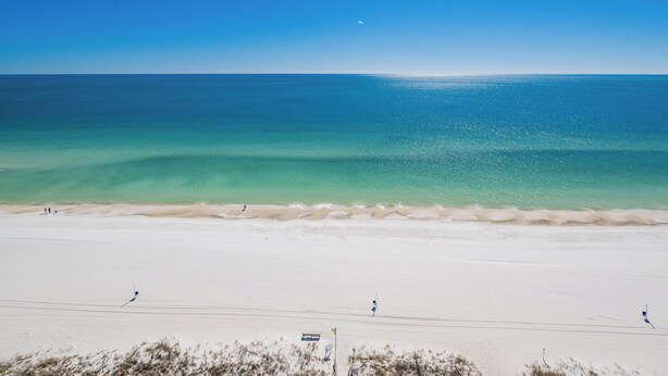 A beach with clear turquoise water, a sandy shore, and a few people in the distance. - Phoenix All Suites West Hotel Unit 301 (Gulf Shores)
