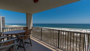 A balcony with a table and chairs overlooking a beach.