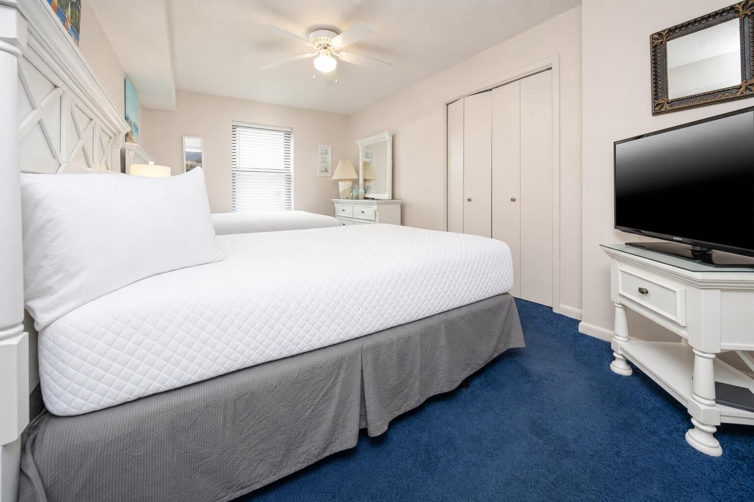 A bedroom with a bed, a television, a dresser, a mirror, and a ceiling fan.