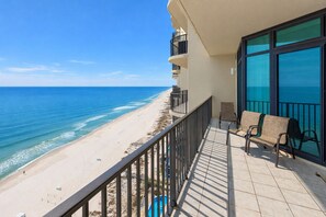 A balcony with a view of the beach and ocean, a pool, and outdoor seating.